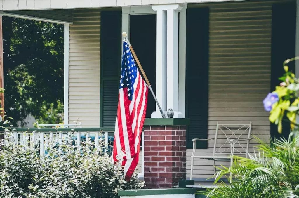 An American flag flying in front of a house from the porch.