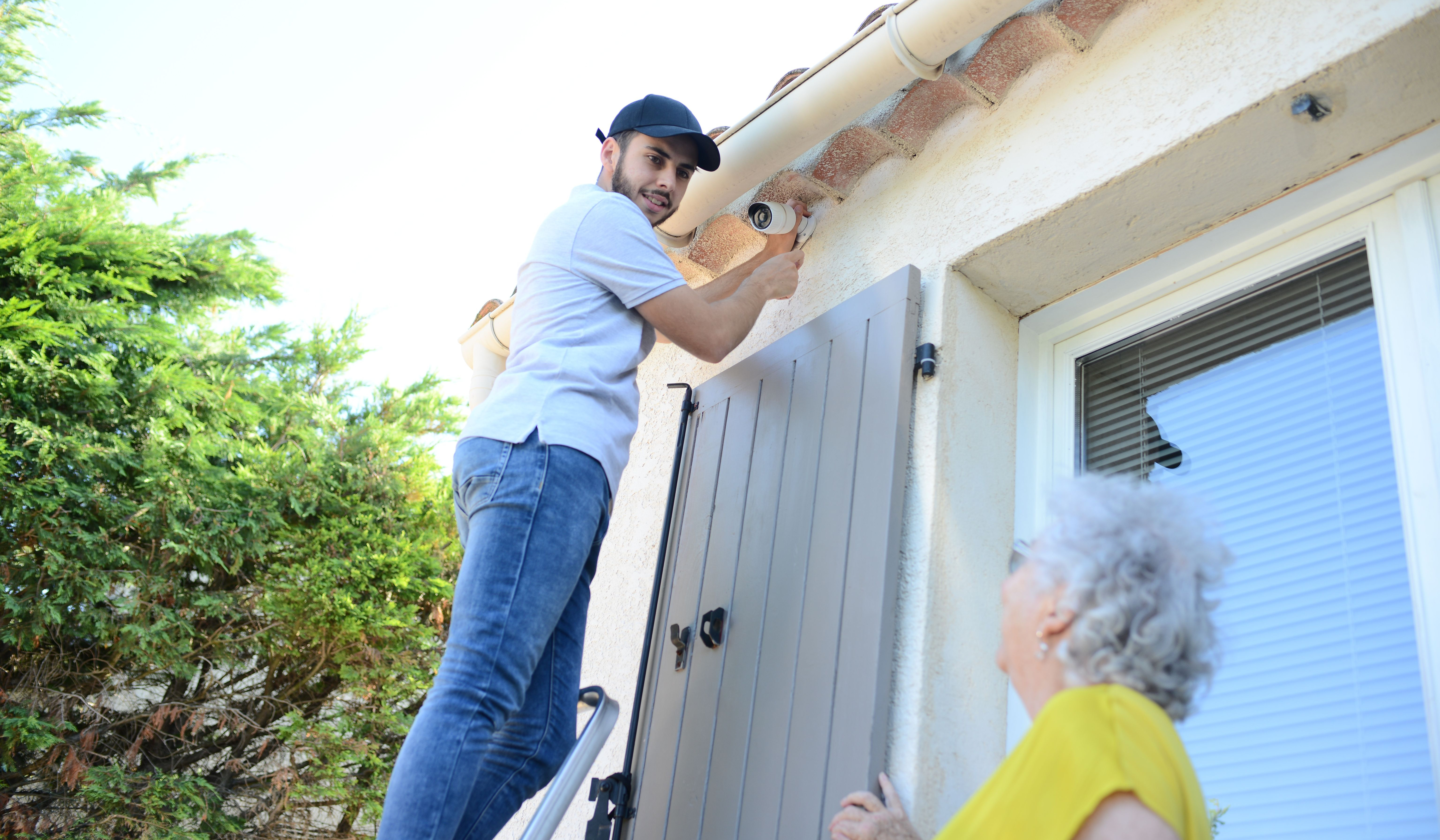 Security specialist installing surveillance cameras around the house while talking to the homeowner